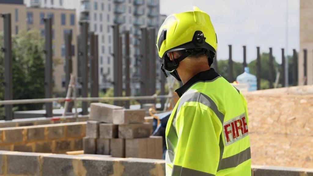 A firefighter wearing a helmet and hi-vis jacket standing by a balcony.
