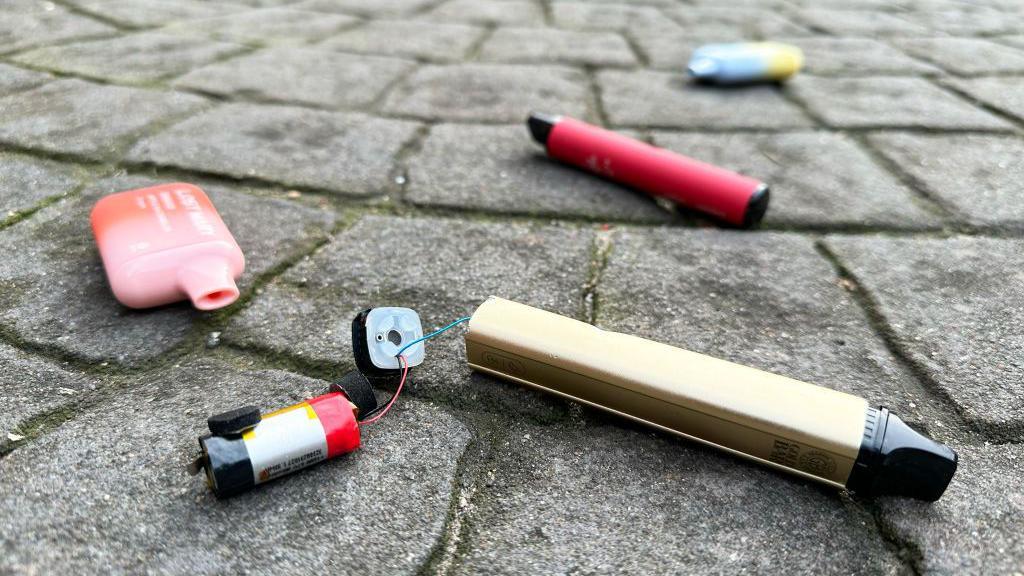 A file image showing a number of discarded disposable vapes in the ground of a carpark in London, including a gold-coloured vape which has split open at the bottom to reveal a battery inside that is wired up to the vape casing