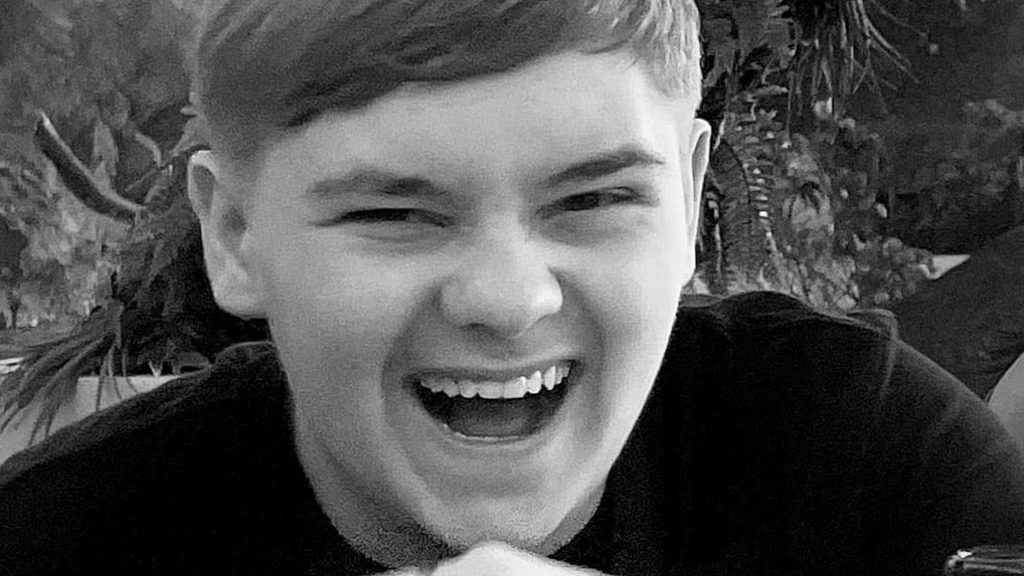 Harvey Willgoose, a teenage boy smiling into the camera. The photograph is monochrome.