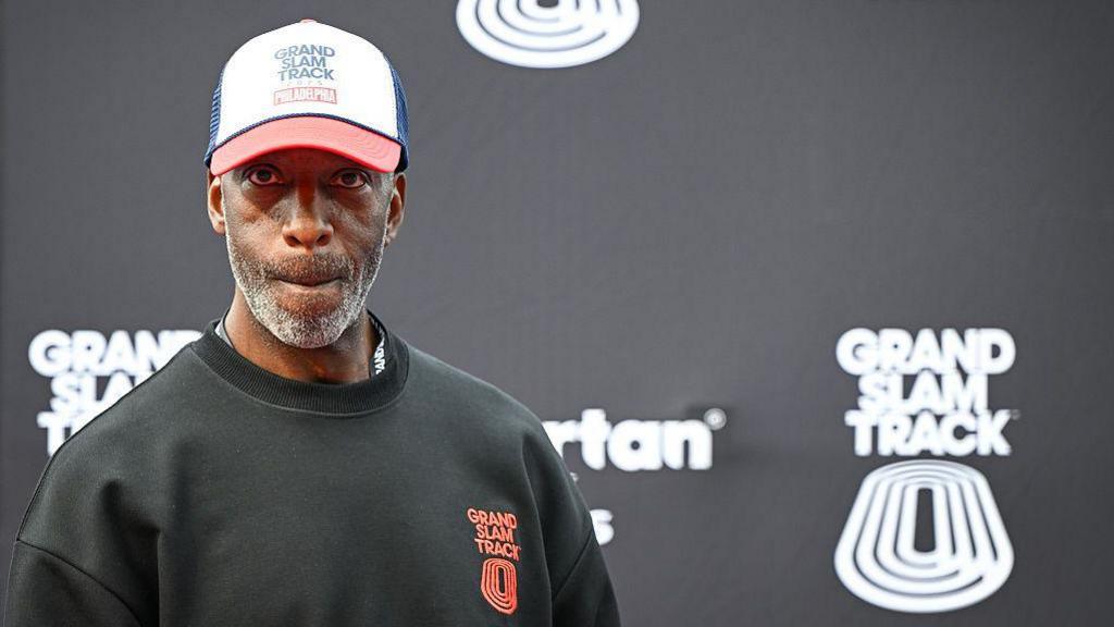 Michael Johnson looking pensive as he stands in front of a black board bearing the Grand Slam Track name and logo