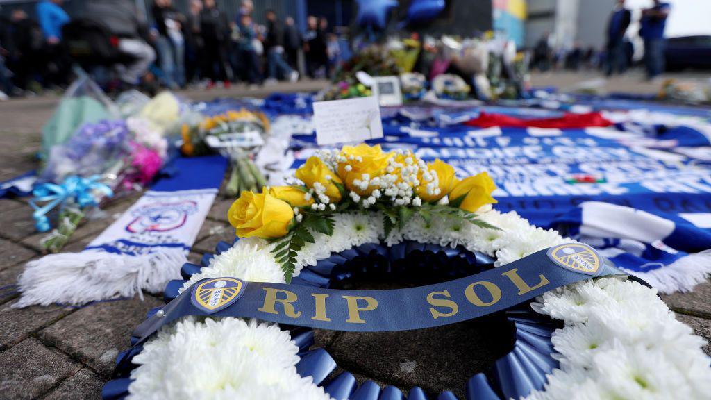 A Leeds United wreath with the words 'RIP Sol' alongside Cardiff scarves and tributes at the base of the Fred Keenor statue at the Cardiff City Stadium