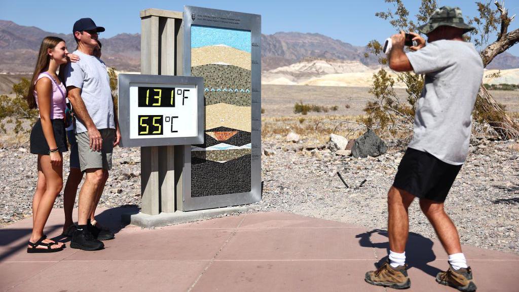 Tourists pose next to thermometer in Death Valley