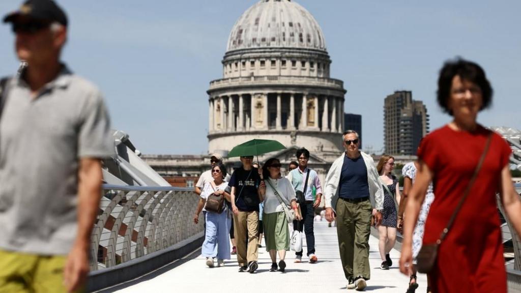 A couple walks with an umbrella along the Millennium Bridge