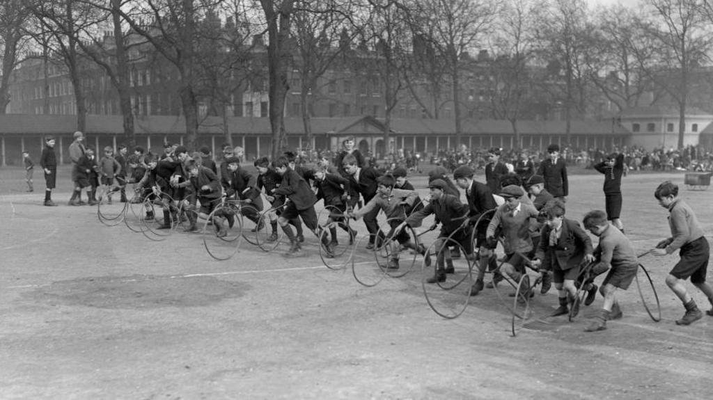 A black and white photo showing a line of boys racing with hoops and sticks in 1931 at the hospital, during a visit by politician George Lansbury