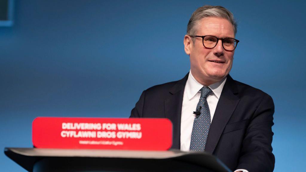 Sir Keir Starmer behind a podium reading Delivering for Wales