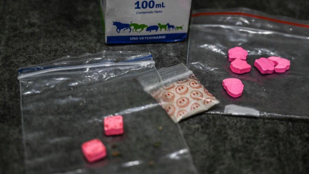 A stock image of some illegal drugs including two bags with pink tablets inside and a bag of white powder in a plastic baggy with smiley faces on