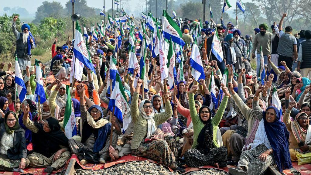 Women farmers are seen protesting on a rail track, with raised green, white and blue flags.

Farmers shouting slogans block railway tracks during a protest against the central government demanding minimum support price (MSP) for their crops, on the outskirts of Amritsar on December 18, 2024. (Photo by Narinder NANU / AFP) (Photo by NARINDER NANU/AFP via Getty Images)
