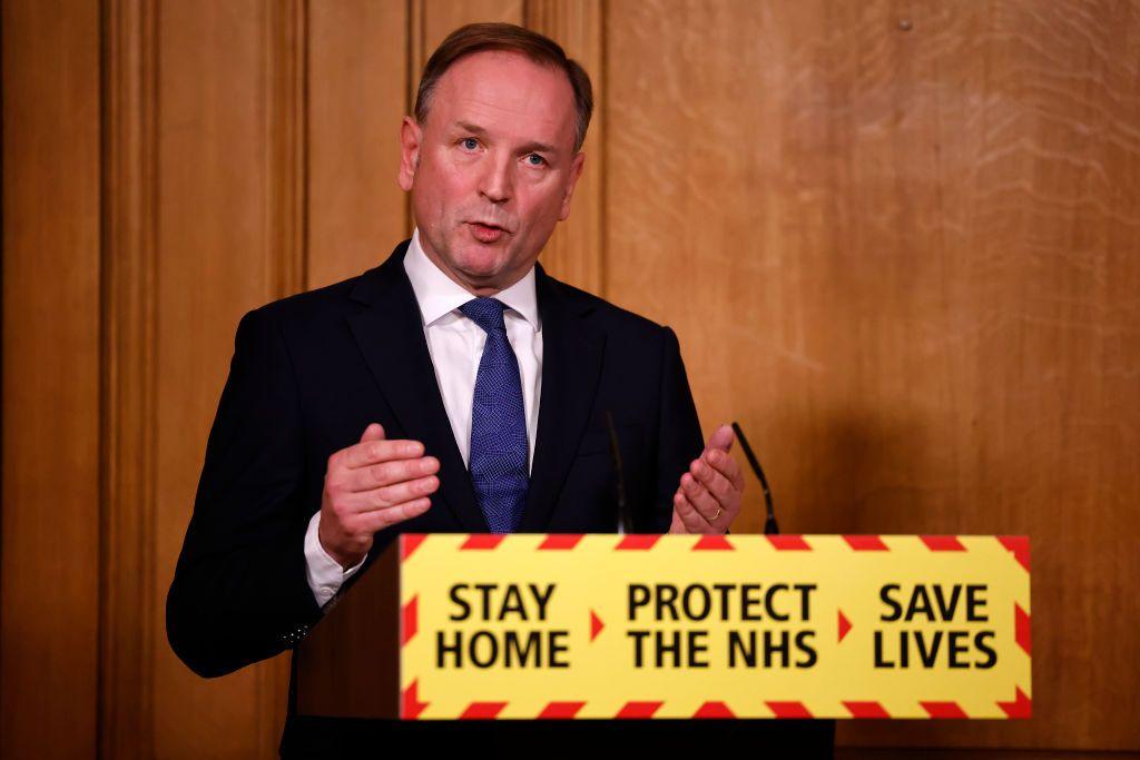 Lord Simon Stevens, a white man wearing at a podium reading 'Stay home; protect the NHS; save lives' during a Covid press conference