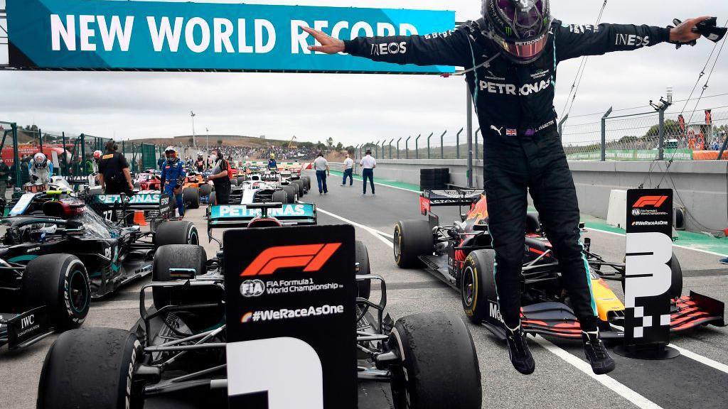 Lewis Hamilton jumps from his Mercedes in celebration after winning the 2020 Portuguese Grand Prix to break the record for F1 wins. An electronic sign in the background says 'New world record'