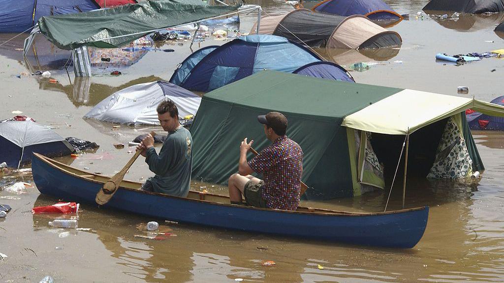 Two men canoe across a flooded campsite at Glastonbury Festival in 2005. Litter and plastic can be seen in the floodwater.
