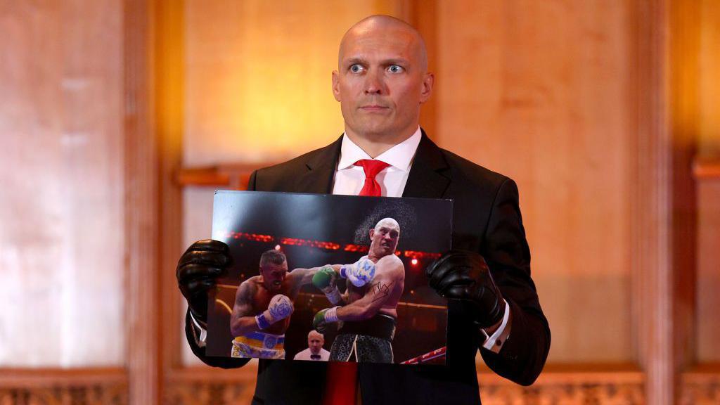 Oleksandr Usyk holds up an autographed picture of him punching Tyson Fury