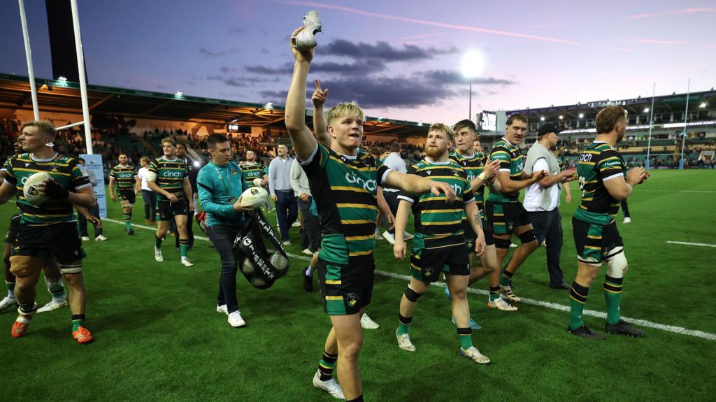 A photo of Henry Pollock holding up his shoe while walking around the pitch at Franklin's Gardens with his team-mates after winning Leicester Tigers in the Prem semi-final on Friday