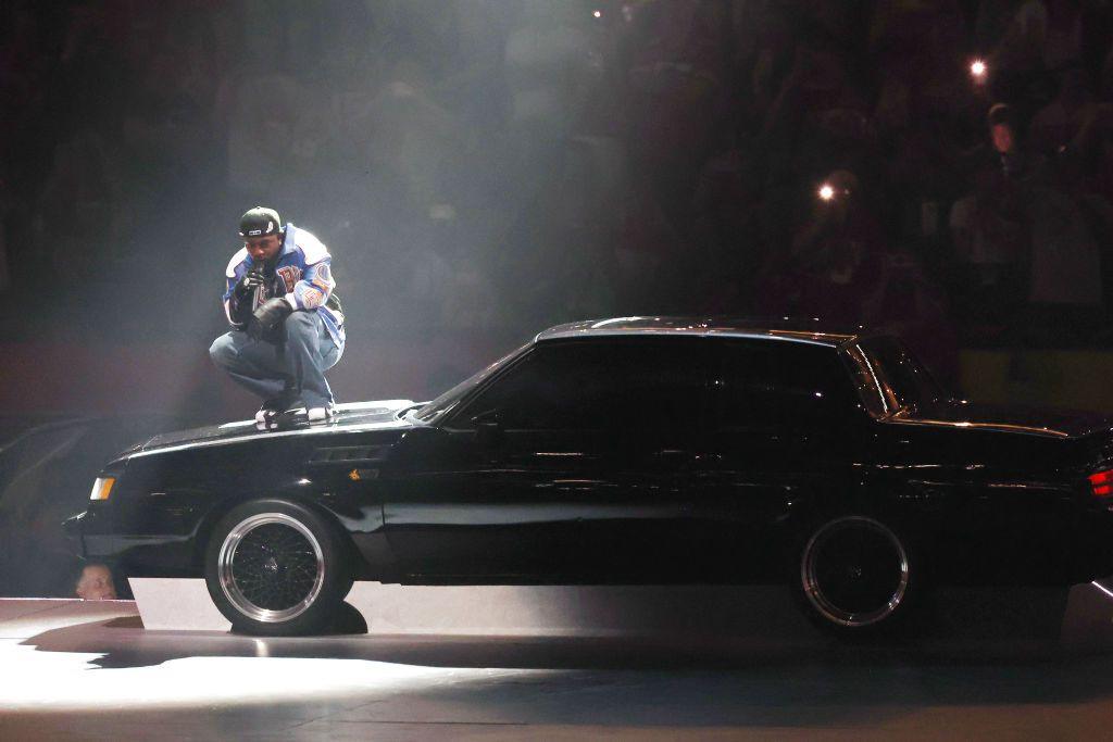 Kendrick Lamar is illuminated by a spotlight while performing on top of the bonnet of a black Buick car at the Super Bowl