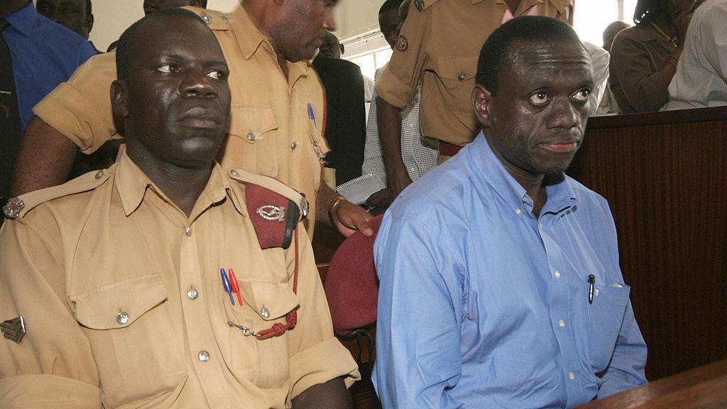 Besigye seated in court wearing a blue shirt in 2005, next to a guard