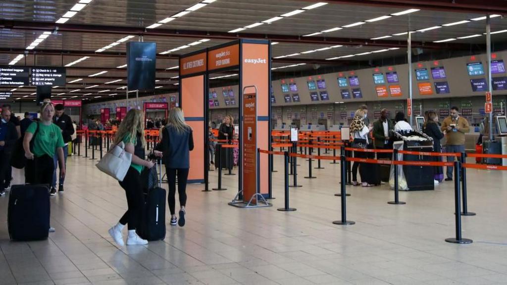 Passengers with suitcases wander London Luton Airport near non-busy check-in desks
