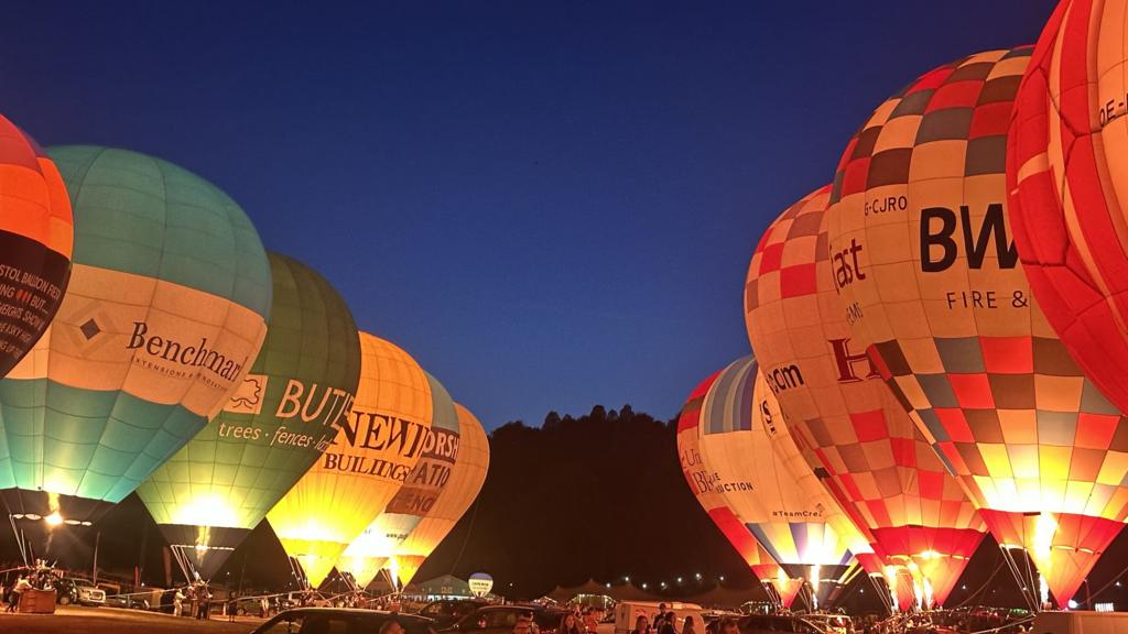 Two lines of hot air balloons light up a dark sky by firing their burners