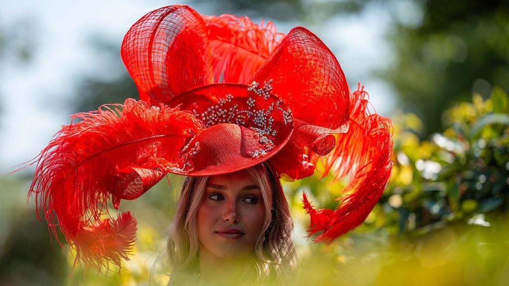 A woman wearing a flamboyant red hat standing for pictures at Royal Ascot on Ladies' Day. 