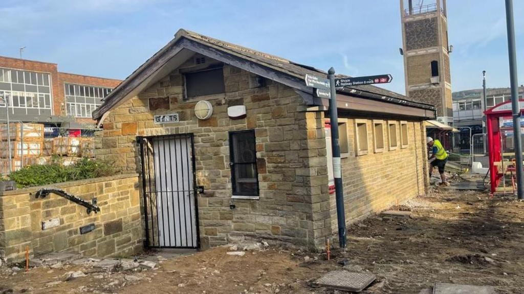 A single story toilet block with a gated doorway and a row of windows along one side