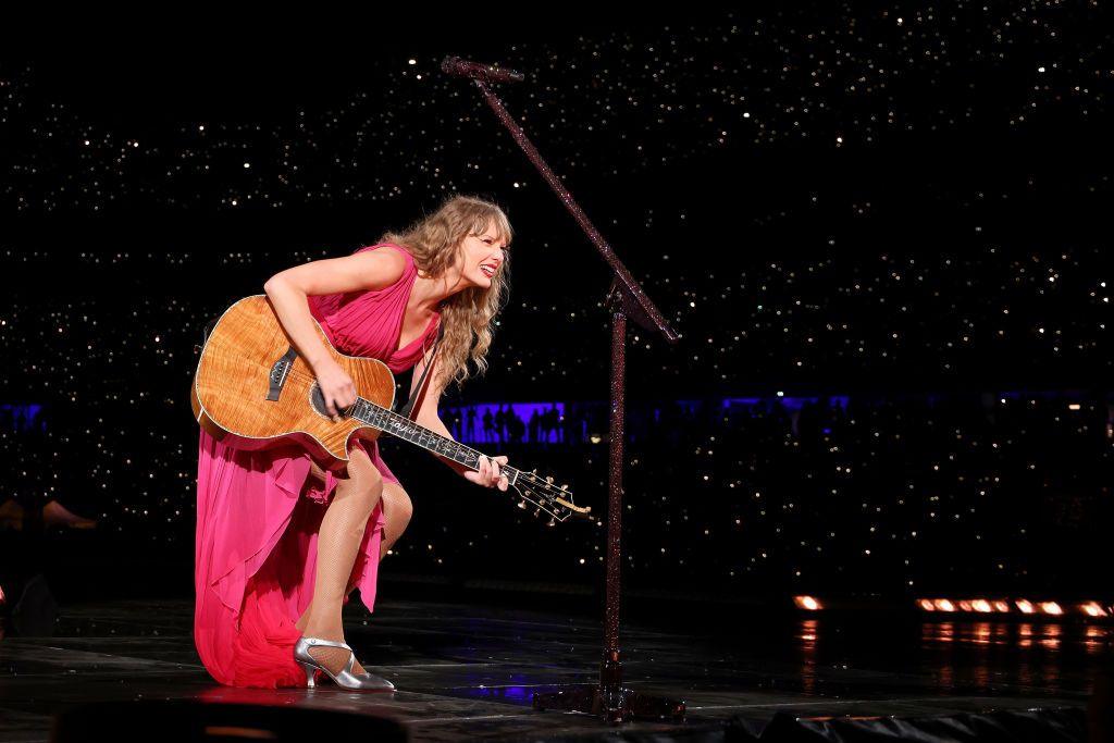 Taylor Swift playing guitar, wearing a pink dress