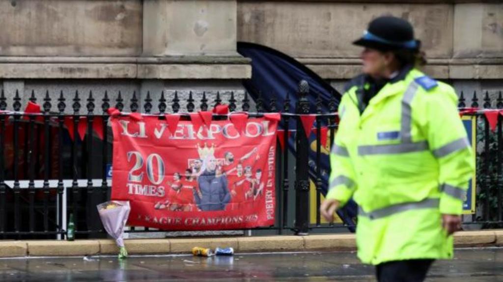 A police officer walks past a Liverpool FC flag at the site of an incident where a car plowed into a crowd of Liverpool fans during a parade celebrating their side's Premier League soccer title, in central Liverpool, Britain