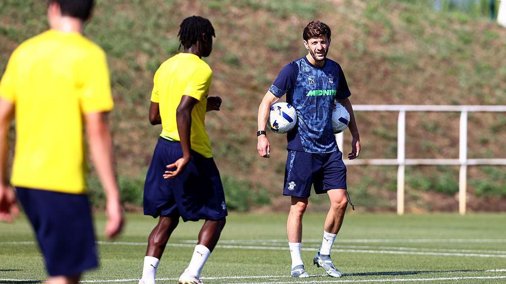 Adam Lallana with a ball under each arm on the coaching pitch