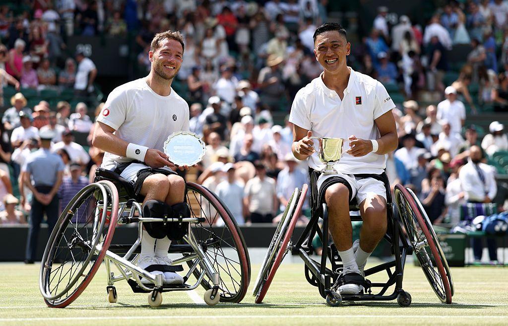 alfie hewett and tokito oda smiling on court one while holding their trophies with a crowd behind them