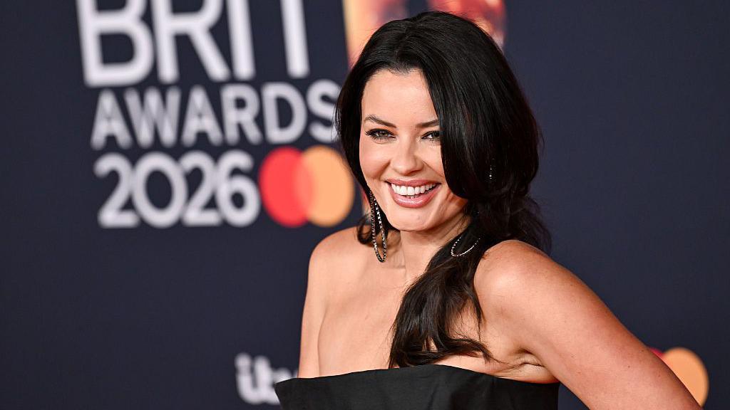A pistillate   with agelong  achromatic  hairsbreadth  is smiling portion    wearing a achromatic  dress. She appears to beryllium  connected  a reddish  carpet astatine  the BRIT awards.