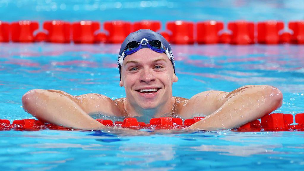  Léon Marchand smiles to the camera from the pool