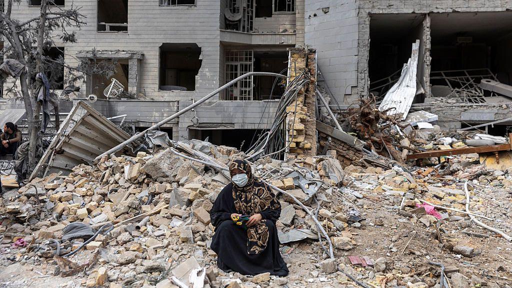  A woman sits amid residential buildings that were destroyed a few days ago following the US and Israeli attack in the eastern Tehran area on March 12, 2026