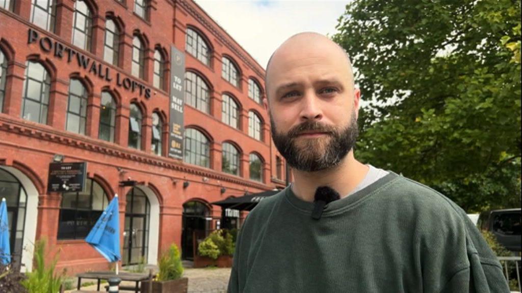 Joe Wagstaff standing outside Pasture in Bristol city centre. He has a dark beard and is wearing a dark grey top