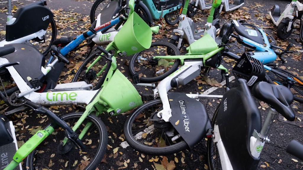 Lime e-bikes and e-scooters and Tier e-bikes parked and fallen across the pavement and street in London