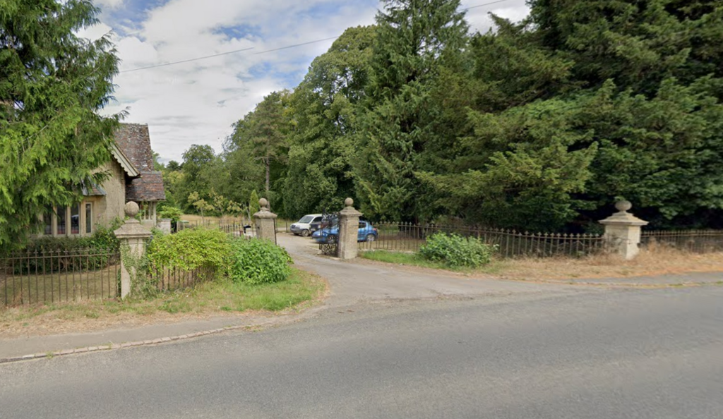 Entrance to estate with trees on either side and cars parked near entrance.