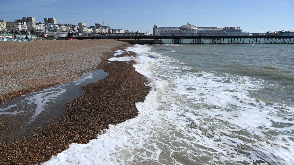 A pebbled-beach with sea foam washing up the shore.