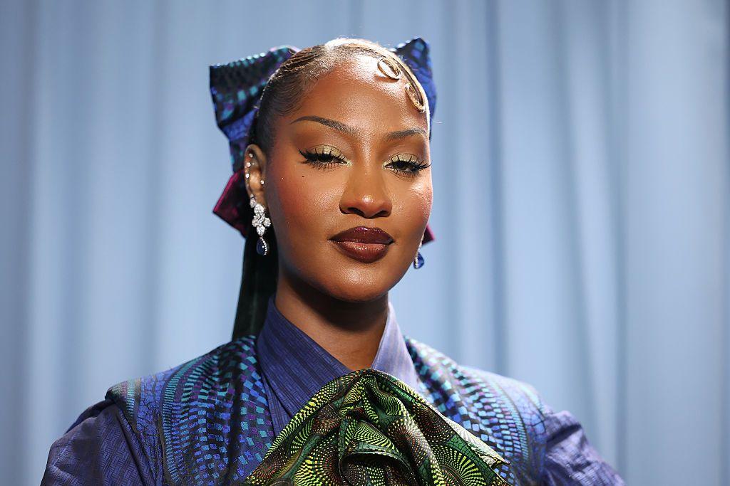 A close up of Tems who is wearing a blue and green African-style outfit.