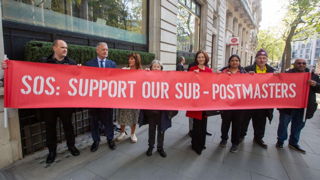 Victims of Post Office scandal hold a banner outside Aldwych House as Angela van den Bogerd starts giving evidence at Post Office - Horizon IT Inquiry