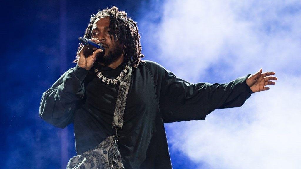 Rapper Kendrick Lamar, wearing black clothes, a necklace, and a bag over his shoulder, holds a microphone as he performs onstage during day three of Rolling Loud Miami 2022 at Hard Rock Stadium on July 24, 2022 in Miami Gardens, Florida