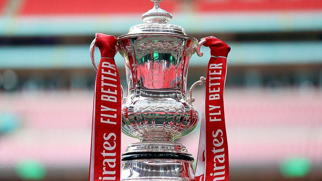The FA Cup trophy, with red ribbons