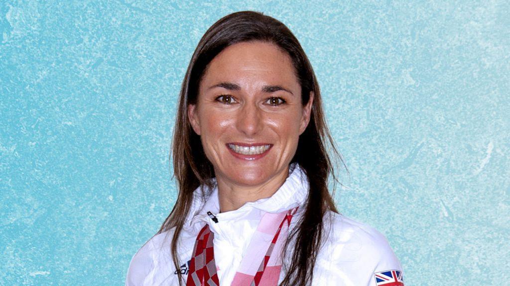 Dame Sarah Storey in her white Team GB Paralympic tracksuit. She has her dark long hair down.