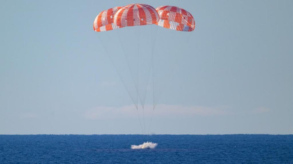 The capsule splashes into the sea with parachutes above it