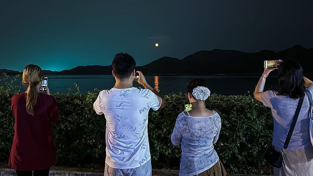 People use smartphones to photograph the full moon rising above the sea and distant hills on May 31, 2026, in Shenzhen, Guangdong Province, China. 