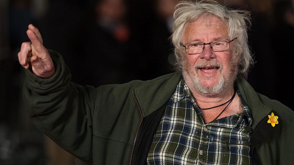 Bill Oddie is photographed crossing his fingers and pointing to the sky