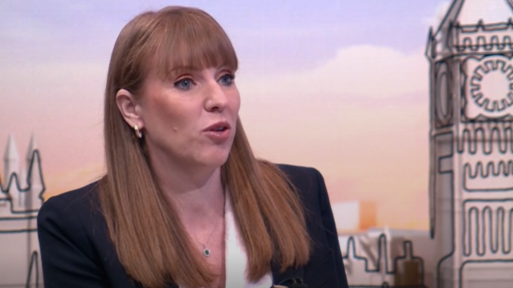 Angela Rayner sitting down during interview. She is wearing a black jacket and white blouse with a small zapphire necklace