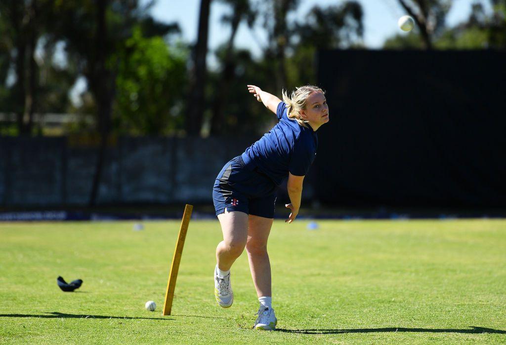 Niamh Muir in a dark blue top and skirt bowls a cricket ball on a perfect flat grass pitch