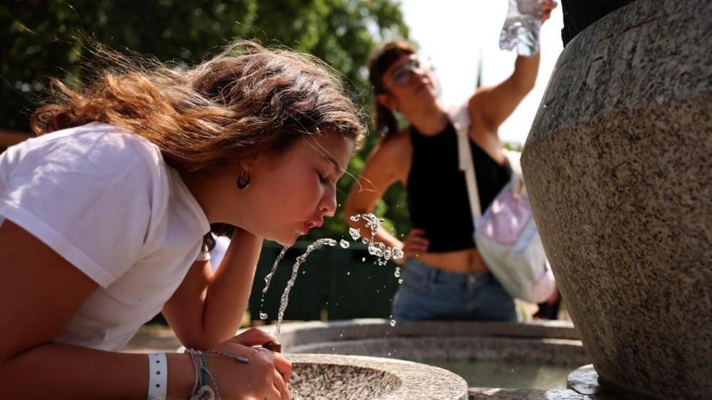 Park goers drink and fill water bottles at a fountain during hot weather in London,