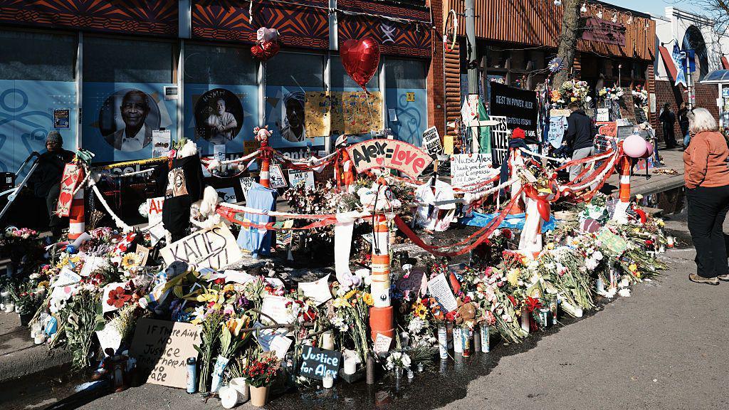 A memorial to Alex Pretti, full of flowers and candles on a sidewalk, set up at the location where federal agents shot and killed him