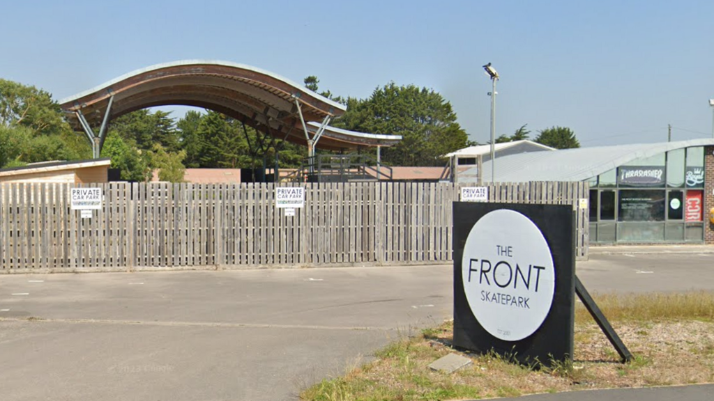 Street view of the skate park entrance, building and car park. The car park is separated from the building by a tall timber fence with signs along it saying private car park.