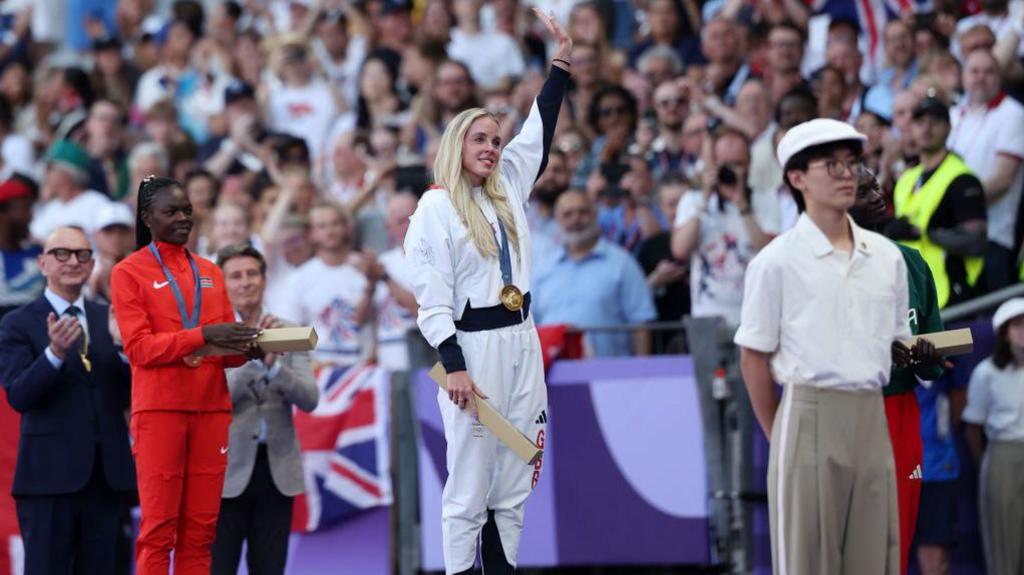 Keely Hodgkinson waves to the crowd standing on the Olympic podium