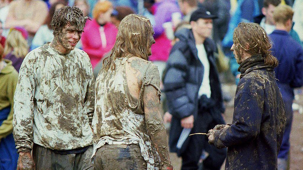 Three festival goers covered from head to toe in mud.