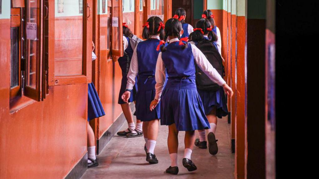 Students play with blue tunics and red hair bands outside their classroom as they wait for their teacher at a school in Imphal, Manipur. 