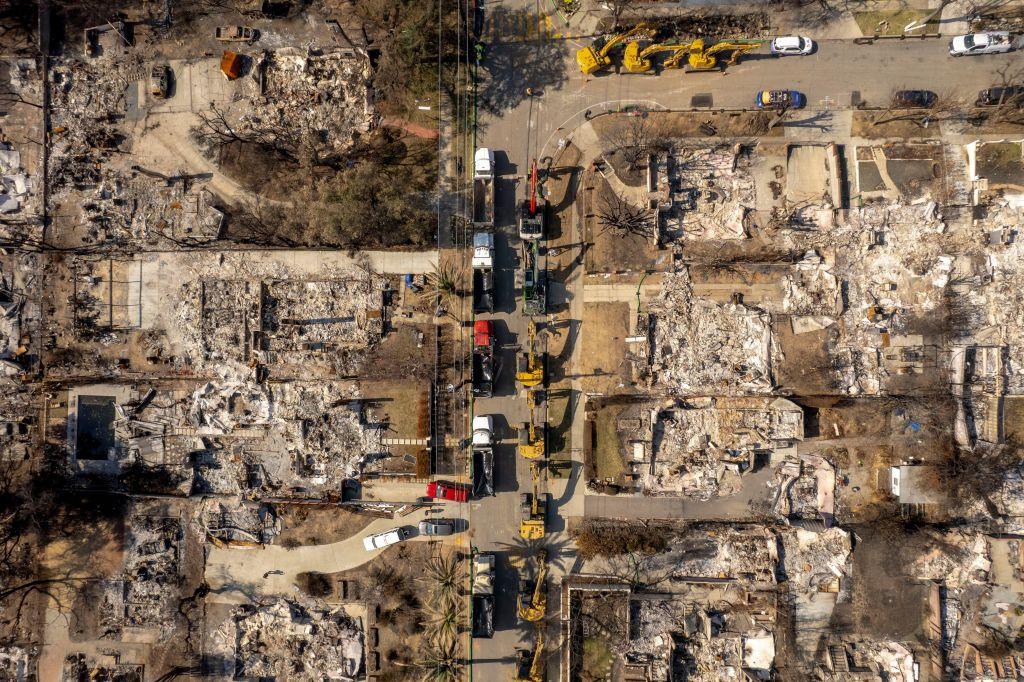 An aerial view of excavation equipment parked alongside destroyed homes